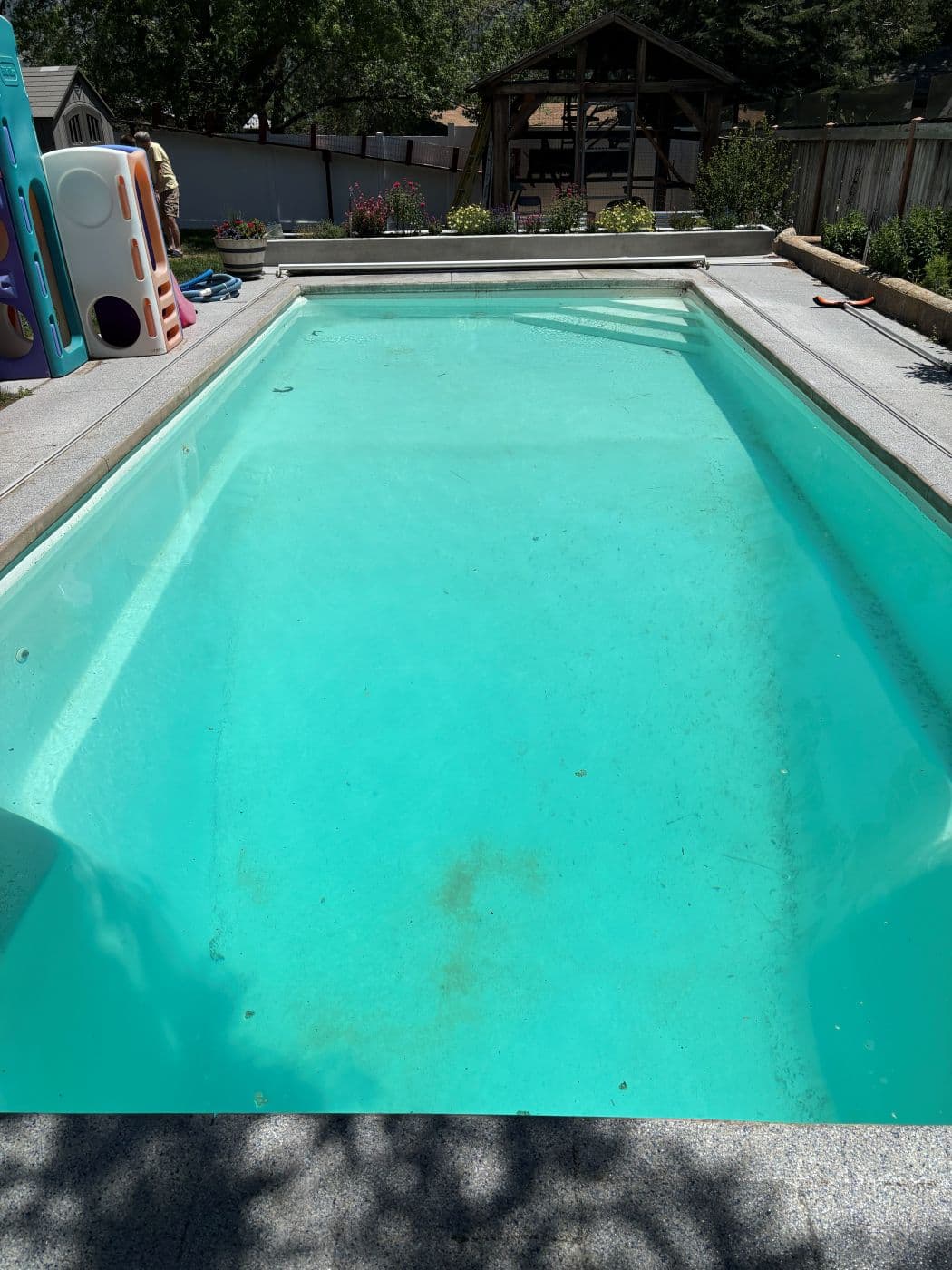 Green murky rectangular pool with the sun cover partway on