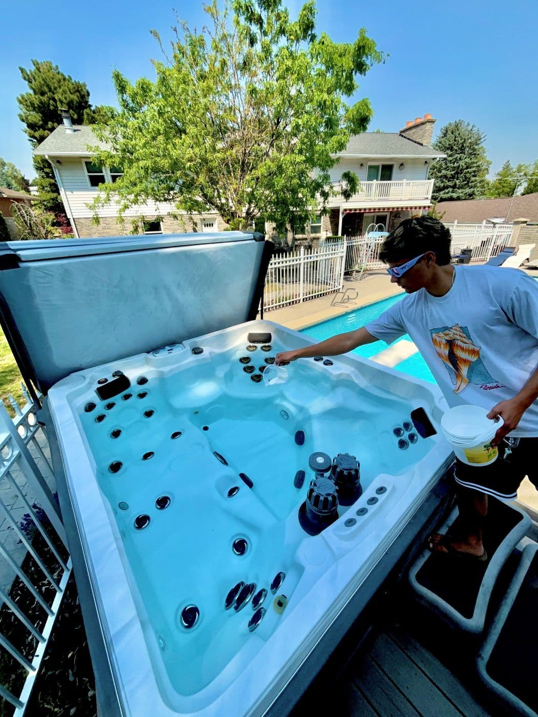 Technician adding chemicals to a hot tub with a pool behind