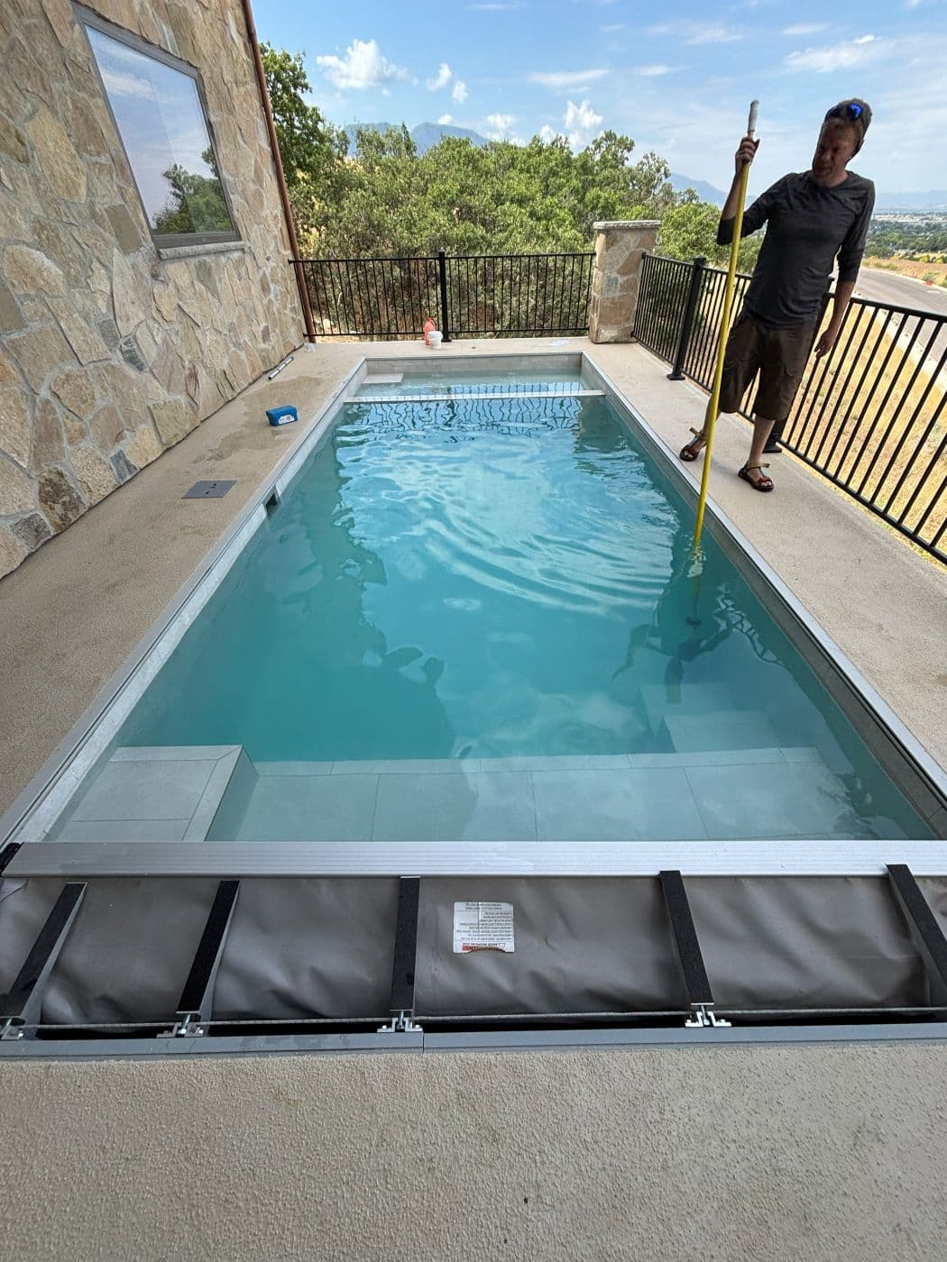 Technician brushing a rectangular pool with a slide and mountain view