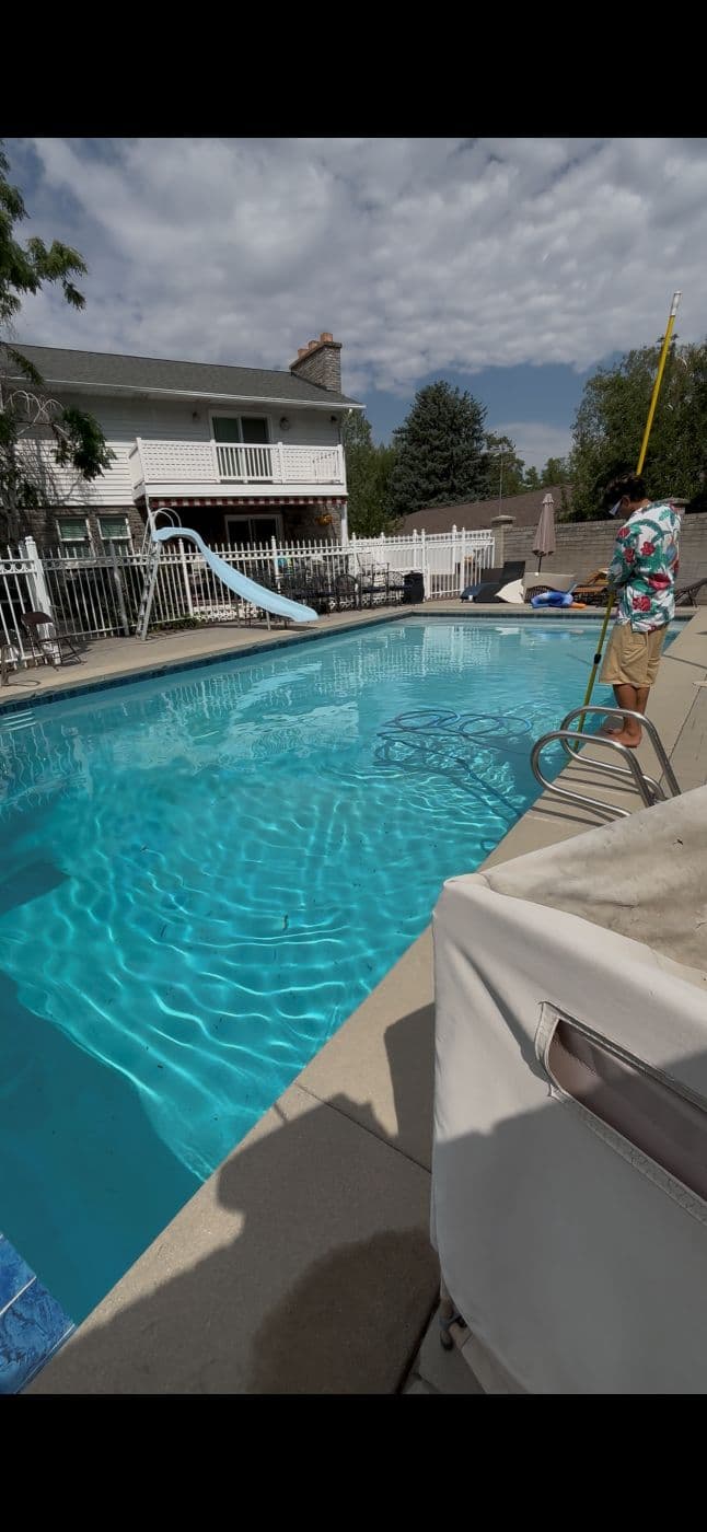 Technician poolside with a pole brush at a pool with a slide