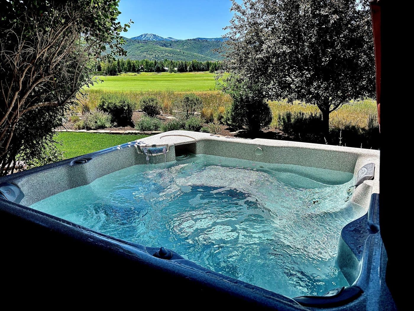 Hot tub with a waterfall feature and a mountain and golf course view